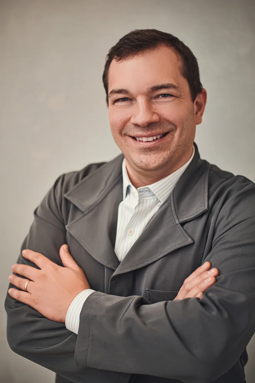 Retrato de Charles Cavalheiro sorrindo, de jaleco cinza e braços cruzados.