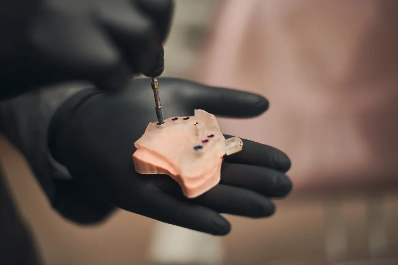 Modelo odontológico de planejamento de implante segurado com luva, com instrumento demonstrativo.
